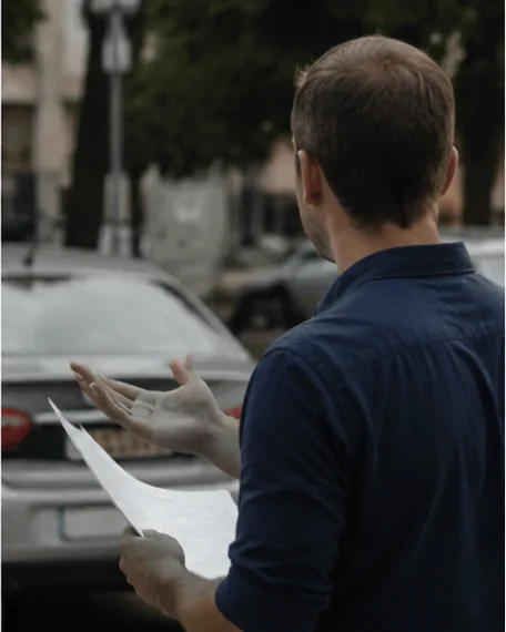 Conductor al lado del auto estacionado, sacándose una duda por teléfono